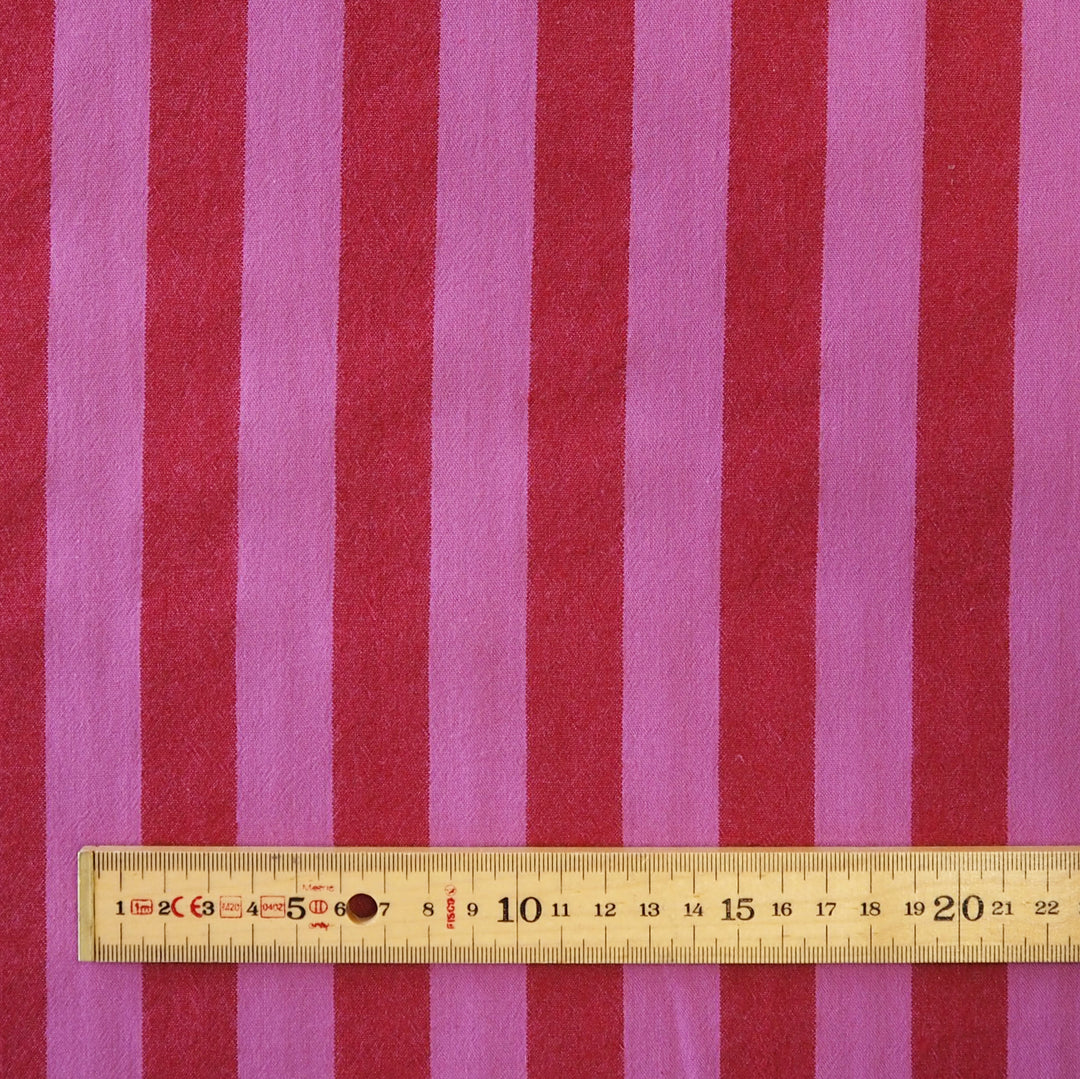 Pink and red vertically striped fabric with a wooden ruler at the bottom for scale.