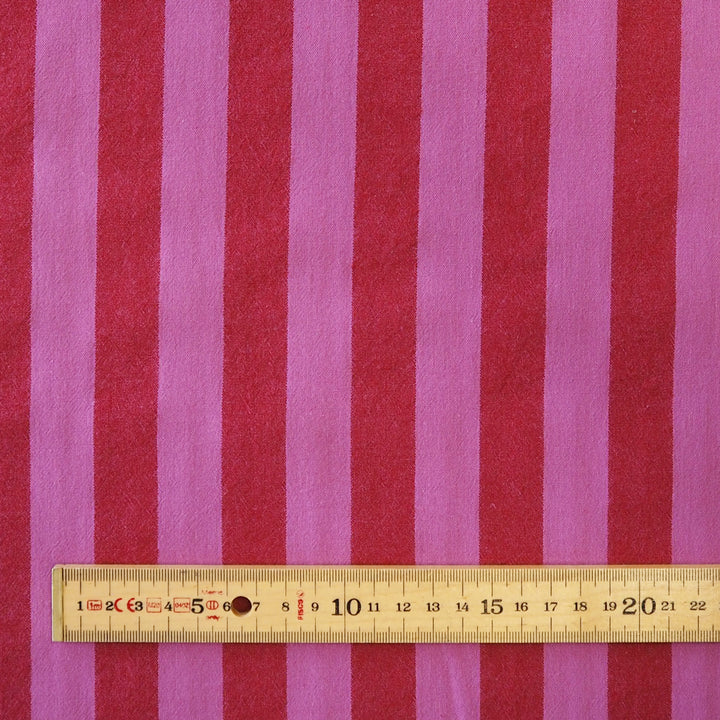 Pink and red vertically striped fabric with a wooden ruler at the bottom for scale.
