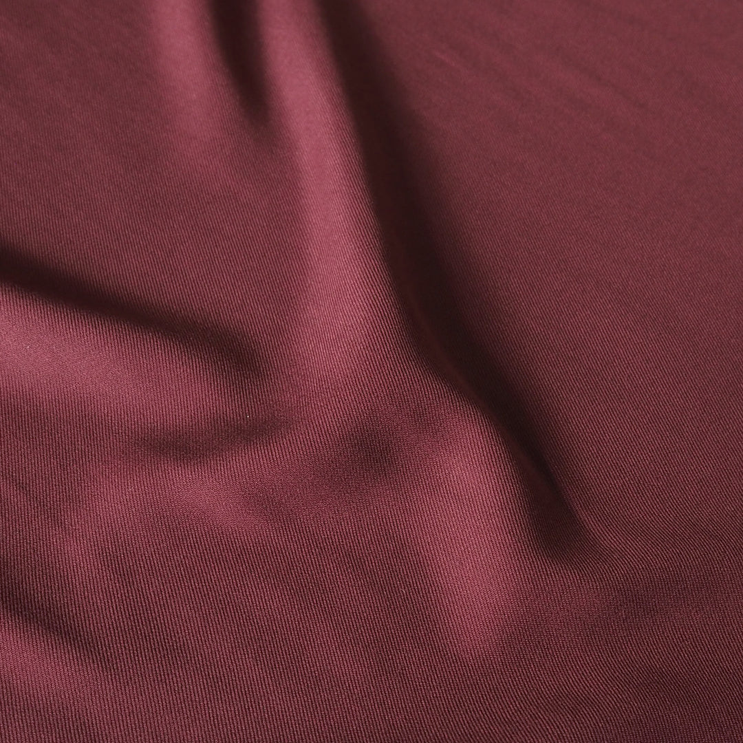 A close-up of draped burgundy fabric with a fine woven texture and soft folds.