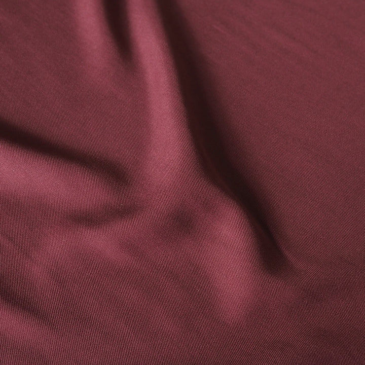 A close-up of draped burgundy fabric with a fine woven texture and soft folds.