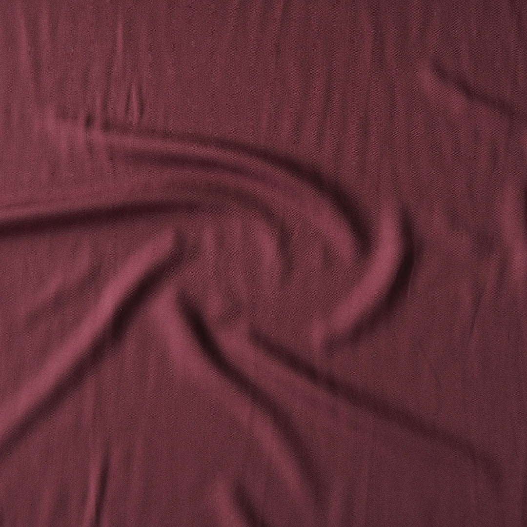 A close-up of draped burgundy fabric with soft folds and a subtle sheen.