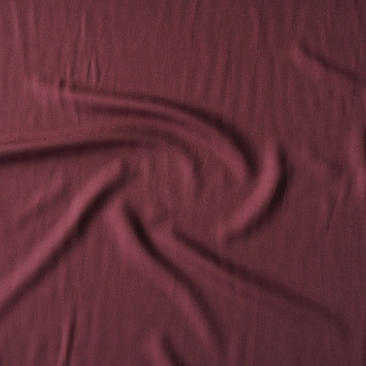 A close-up of draped burgundy fabric with soft folds and a subtle sheen.