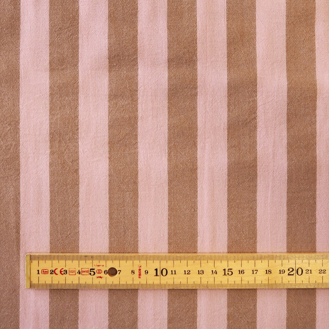 Brown and light pink vertically striped fabric with a yellow measuring tape ruler laid horizontally for scale.
