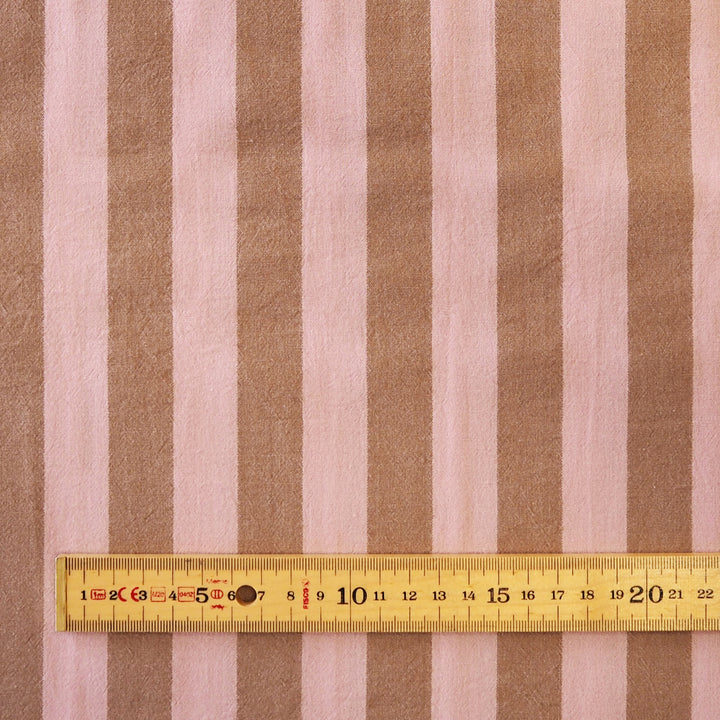 Brown and light pink vertically striped fabric with a yellow measuring tape ruler laid horizontally for scale.