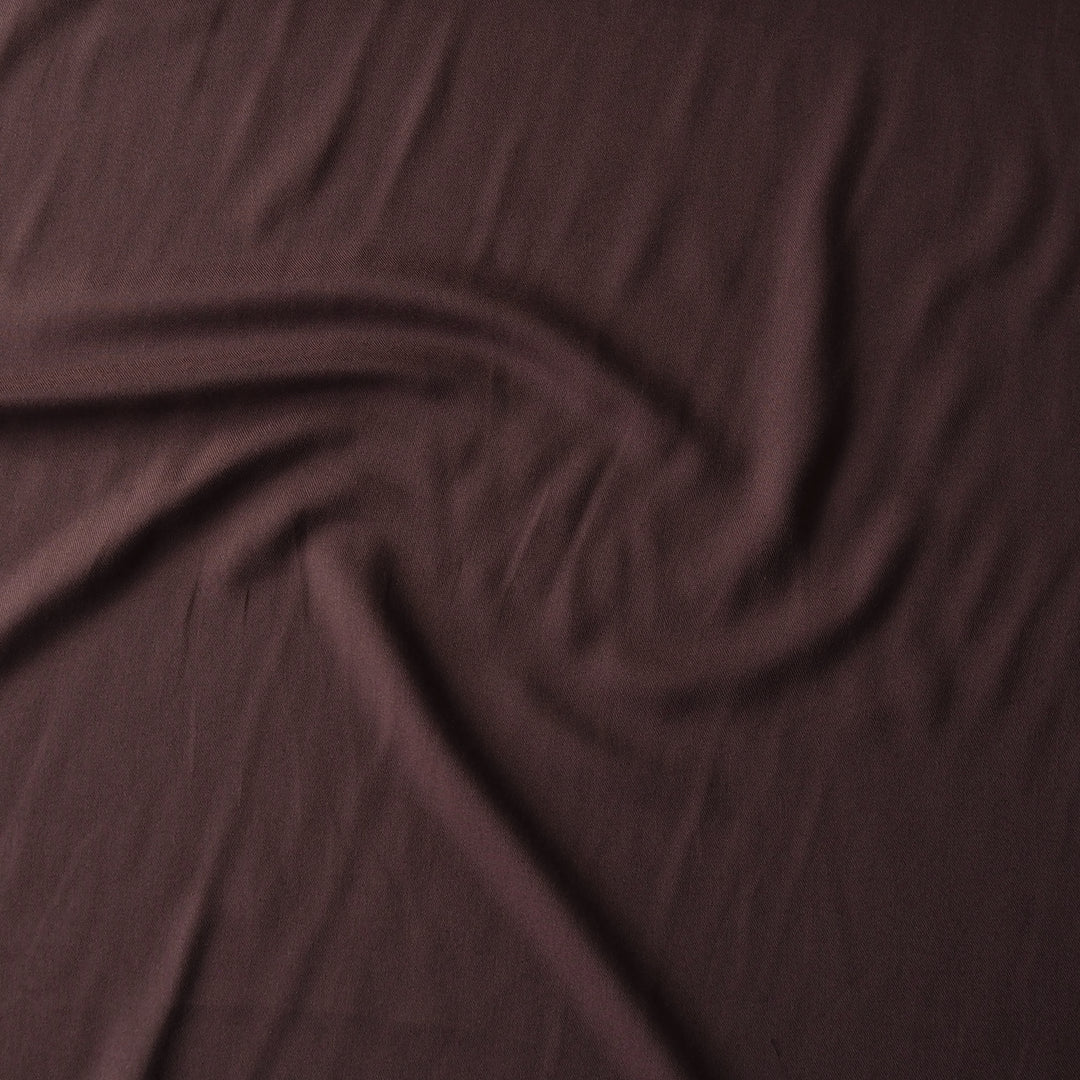A close-up of draped chocolate brown fabric with soft folds and a subtle sheen.