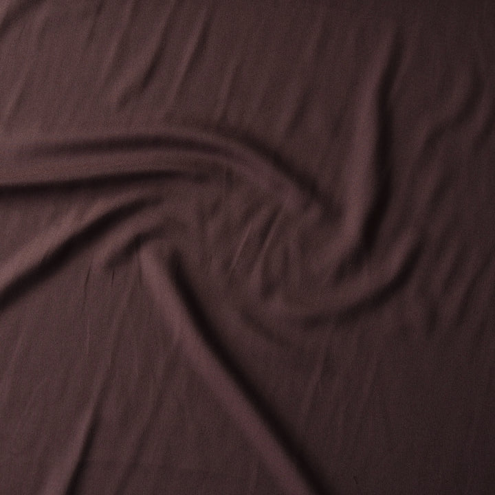 A close-up of draped chocolate brown fabric with soft folds and a subtle sheen.