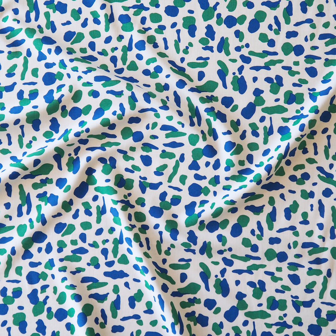 A close-up of draped fabric with an all-over abstract spotted pattern in blue and green on a white background.
