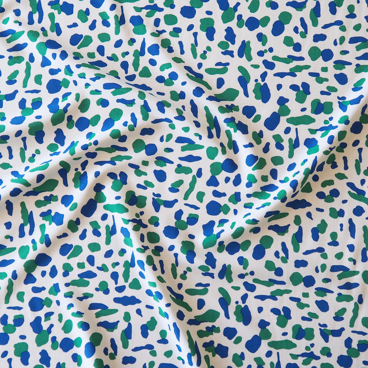 A close-up of draped fabric with an all-over abstract spotted pattern in blue and green on a white background.