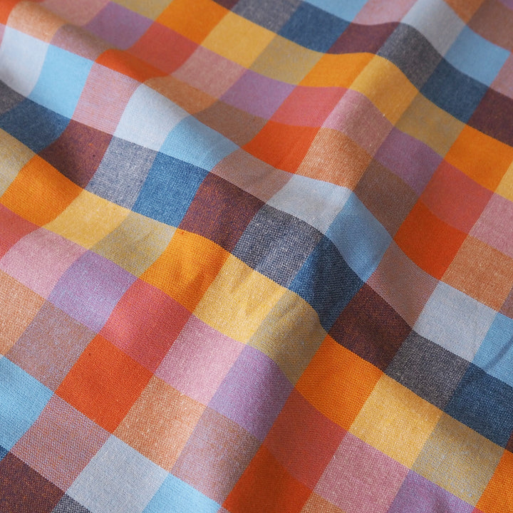 A close-up of a plaid fabric with a multicolor checkered pattern including orange, yellow, blue, pink, purple, and brown.