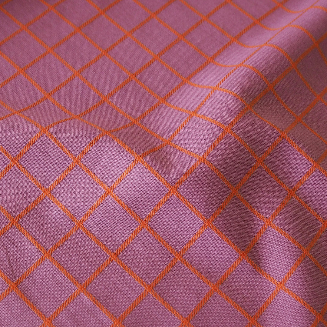 A close-up of a woven fabric with a dusty purple base and a bright orange diamond grid pattern.