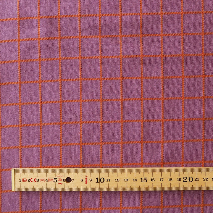Purple fabric with an orange grid pattern, shown with a wooden ruler at the bottom to indicate scale.