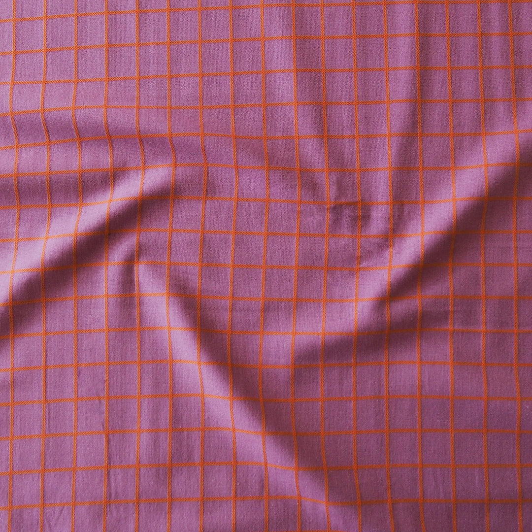 A close-up of a purple fabric with a red-orange grid pattern, showing soft folds and texture.
