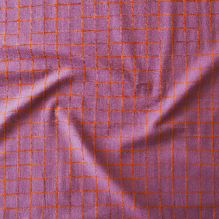 A close-up of a purple fabric with a red-orange grid pattern, showing soft folds and texture.