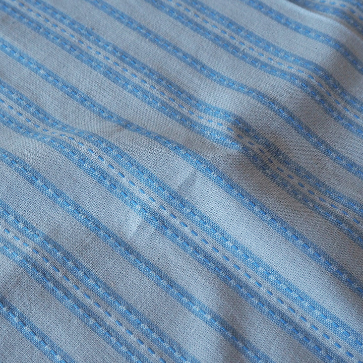 A close-up of a light blue and white striped fabric with a textured weave and stitched stripe details.