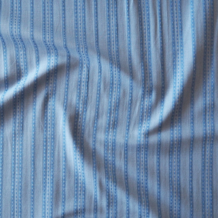 Light blue and medium blue striped fabric with a subtle woven texture and vertical dashed lines.