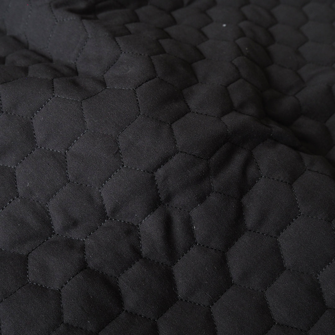 Close-up of a black quilted fabric with a repeating hexagonal stitched pattern.