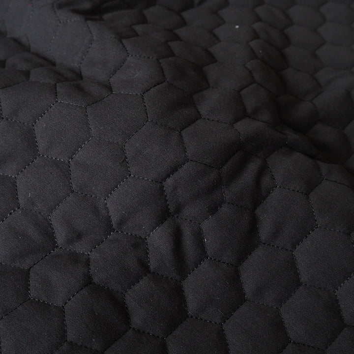 Close-up of a black quilted fabric with a repeating hexagonal stitched pattern.