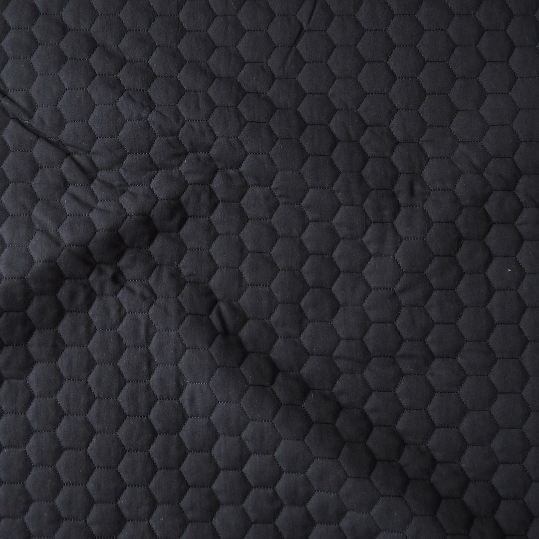 Close-up of a dark charcoal gray quilted fabric with a repeating hexagonal stitched pattern.