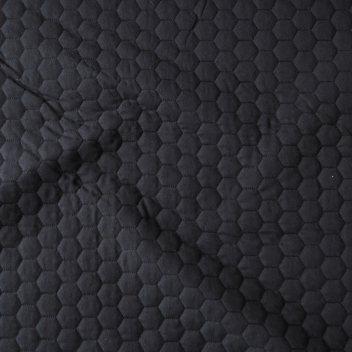 Close-up of a dark charcoal gray quilted fabric with a repeating hexagonal stitched pattern.