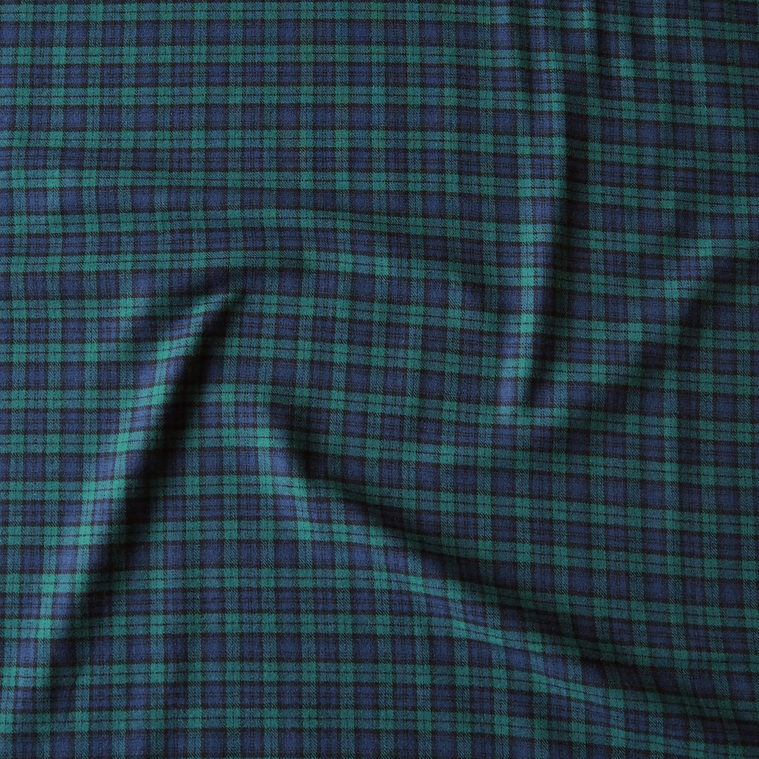 A close-up of a plaid fabric with a green and dark blue pattern, showing soft folds and texture.