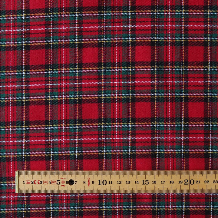 Red tartan plaid fabric with black, green, and white stripes, shown with a wooden ruler at the bottom to indicate scale.