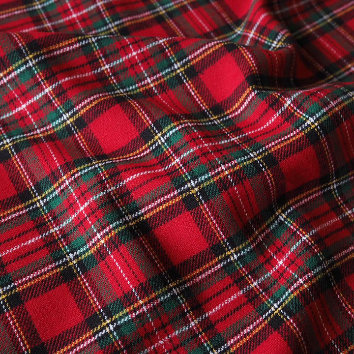 A close-up of red tartan plaid fabric with black, green, white, and thin yellow stripes forming a classic plaid pattern.
