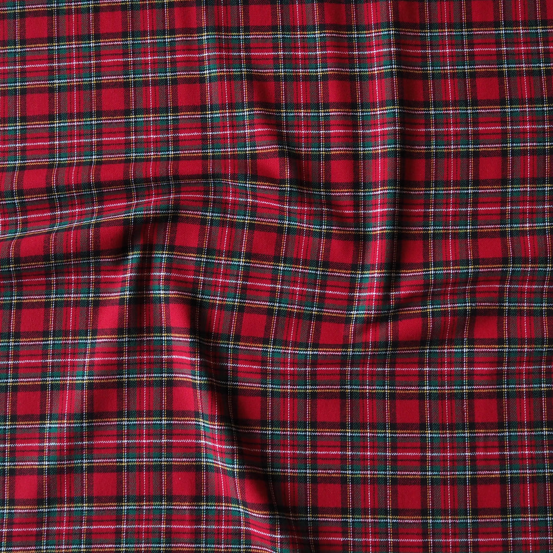 Red plaid fabric with black and thin green stripes, shown with soft folds and wrinkles.