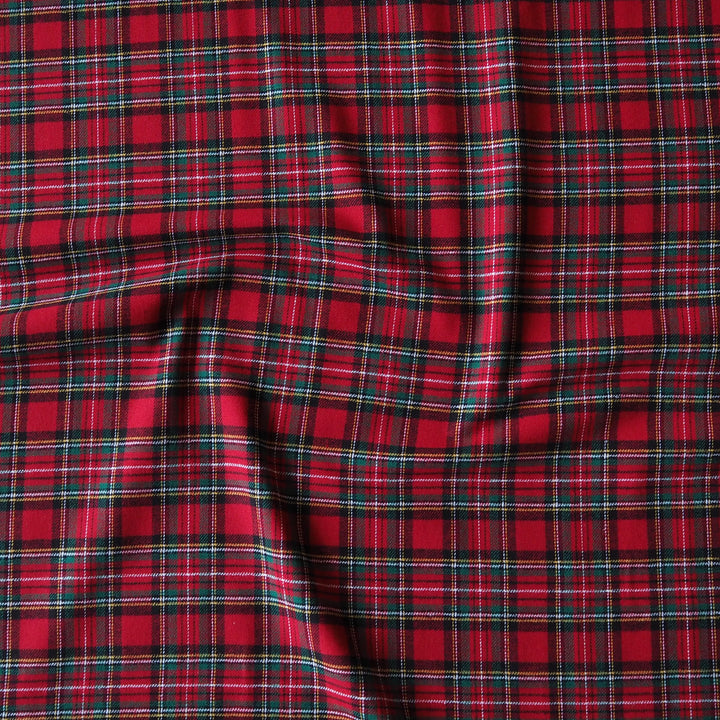 Red plaid fabric with black and thin green stripes, shown with soft folds and wrinkles.