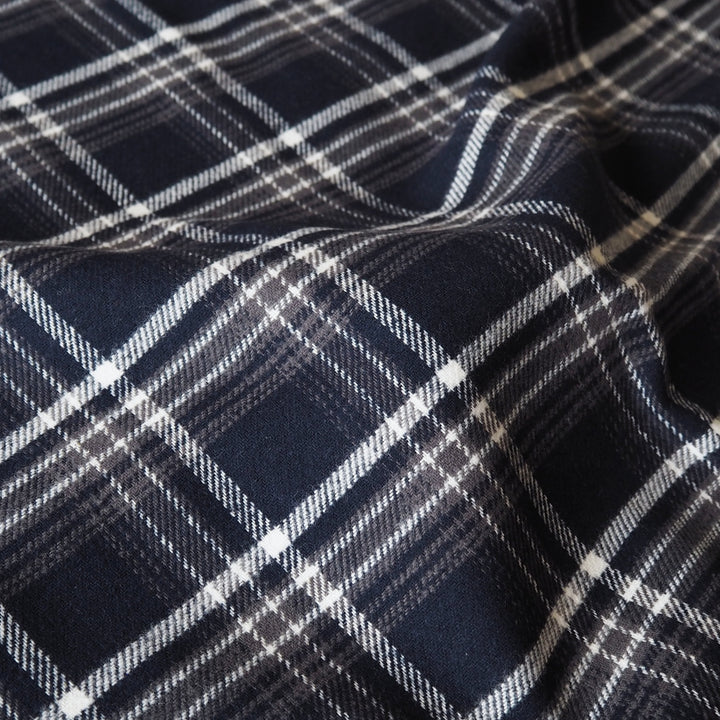 A close-up of a navy blue plaid fabric with white and gray diagonal stripes, showing a soft draped texture.