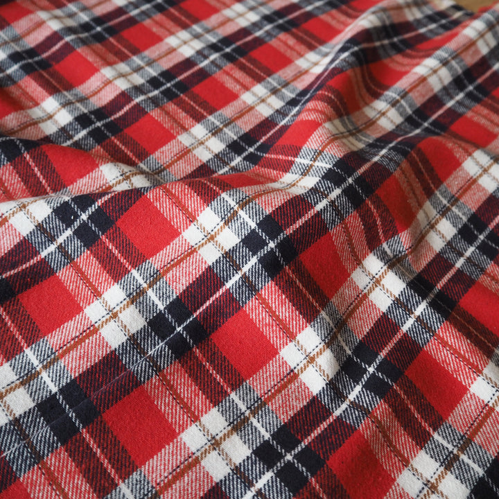 Red plaid fabric with black, white, and thin brown stripes, shown in soft folds.