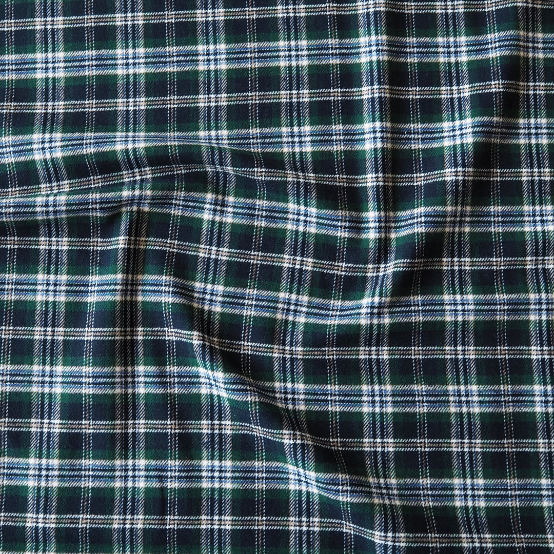 A close-up of a dark green plaid fabric with white and light blue intersecting stripes, showing a soft draped texture.