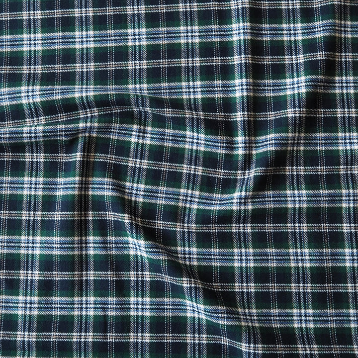 A close-up of a dark green plaid fabric with white and light blue intersecting stripes, showing a soft draped texture.