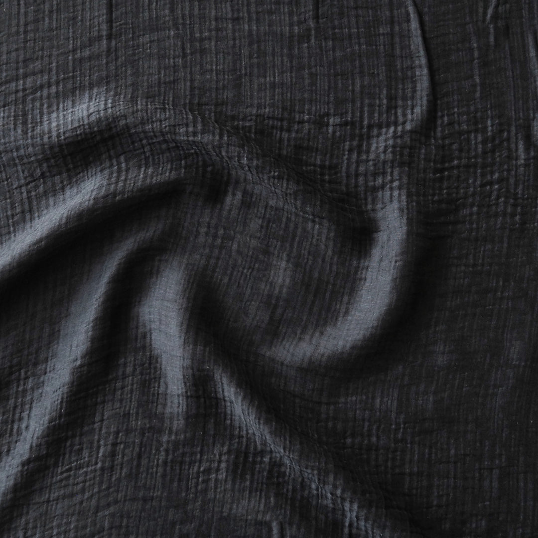 A close-up of dark black crinkled fabric with soft folds and a textured gauze-like surface.