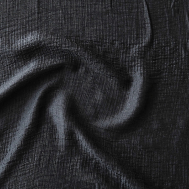 A close-up of dark black crinkled fabric with soft folds and a textured gauze-like surface.