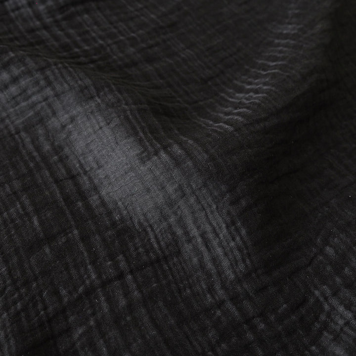 A close-up of a dark black crinkled fabric texture with soft folds and a matte finish.
