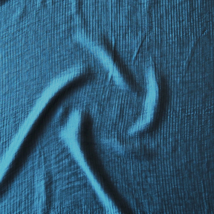 A close-up of textured blue fabric with a crinkled, gauze-like surface and soft folds.