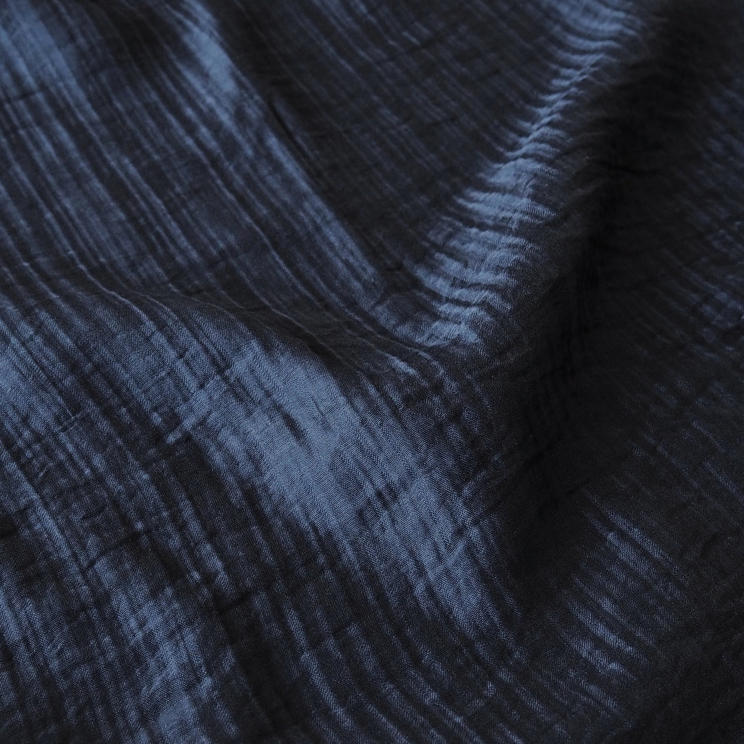 A close-up of dark navy blue crinkled fabric with a textured, crisscross pattern and soft folds.