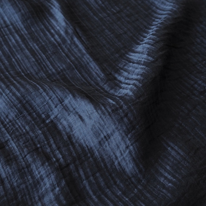 A close-up of dark navy blue crinkled fabric with a textured, crisscross pattern and soft folds.