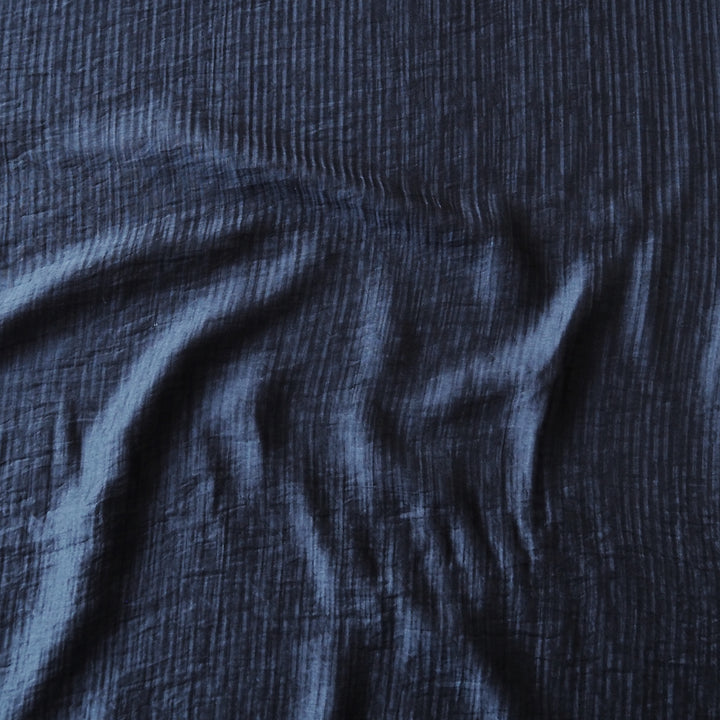 A close-up of dark navy blue crinkled fabric with soft folds and a textured weave.