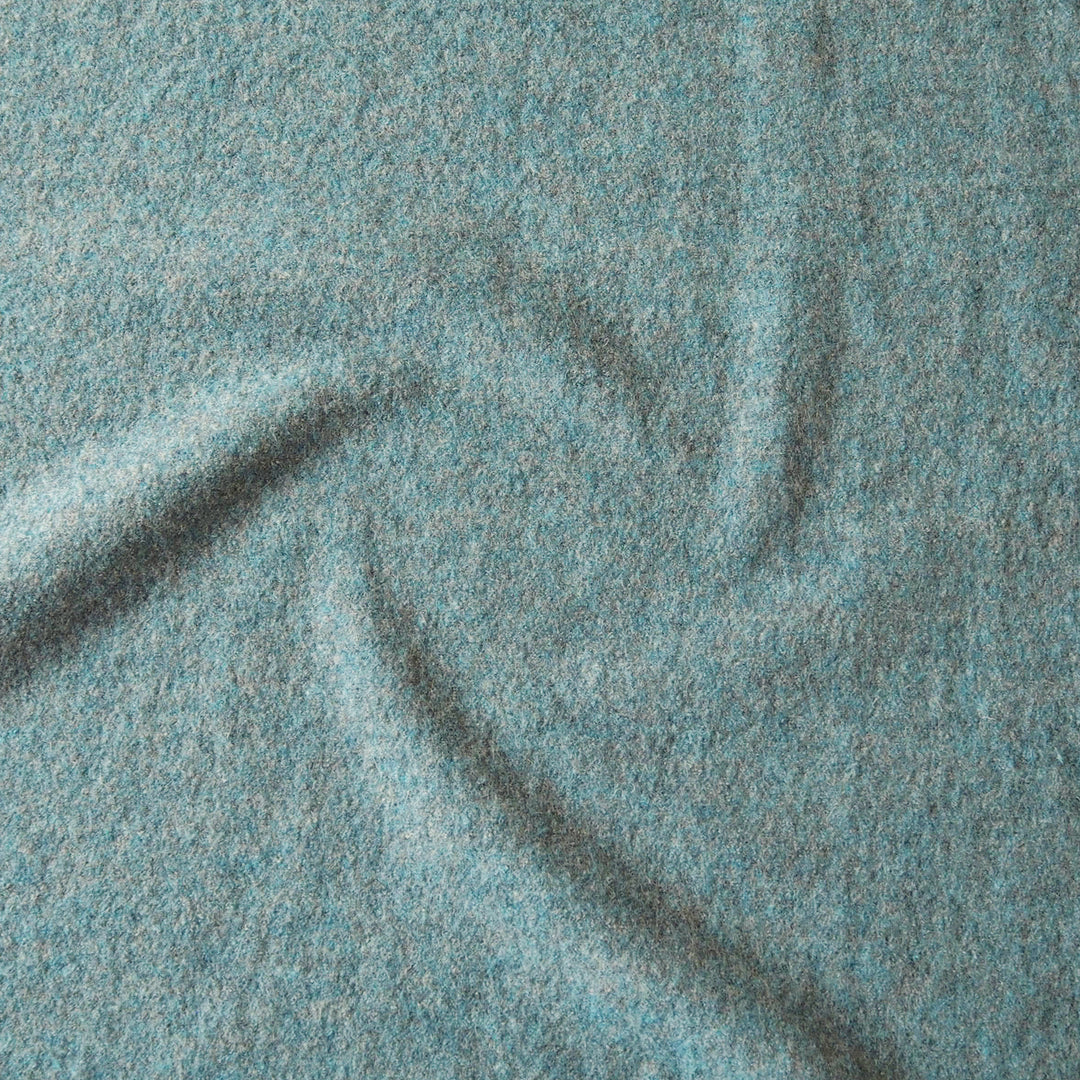 A close-up of textured fabric in a heathered light blue-gray color, showing soft folds and a woven surface.