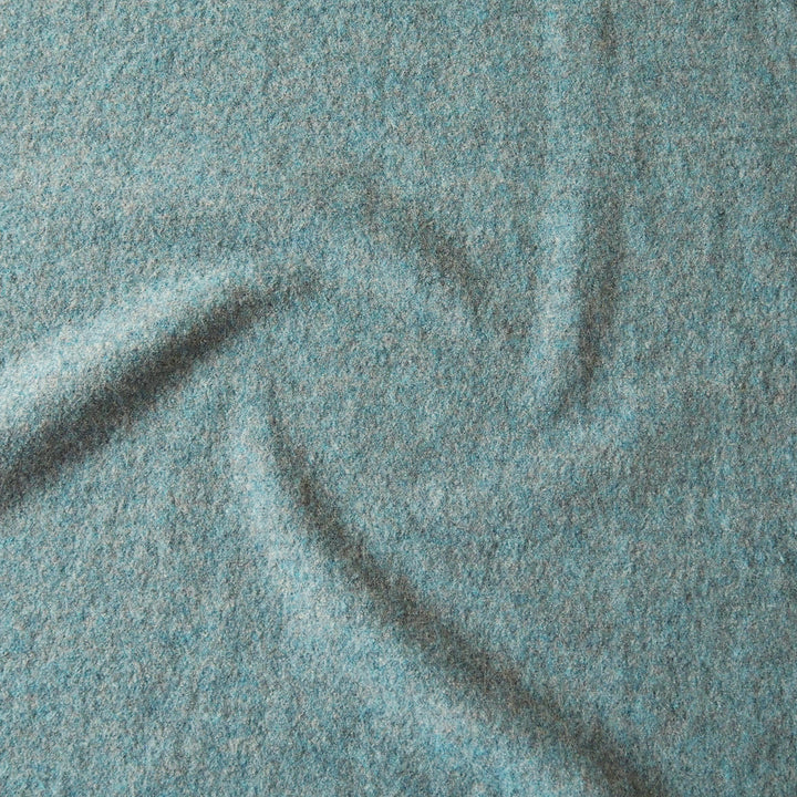 A close-up of textured fabric in a heathered light blue-gray color, showing soft folds and a woven surface.
