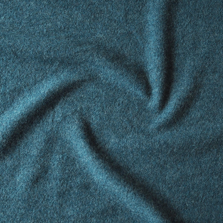 A close-up of textured fabric in a muted teal-blue color, shown with soft folds and shadows.