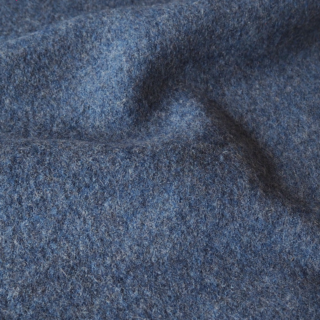 A close-up of textured blue-gray wool fabric with soft folds and a heathered, felt-like surface.