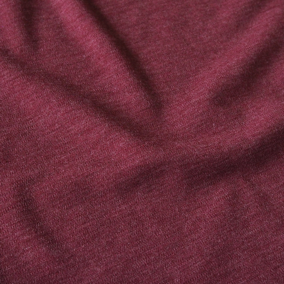 A close-up of draped heathered burgundy fabric with soft folds and a fine knit texture.