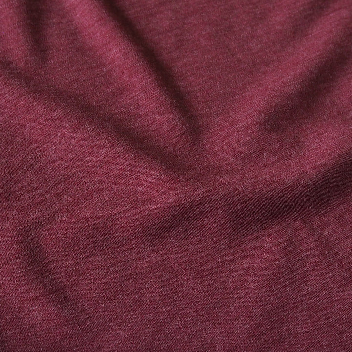 A close-up of draped heathered burgundy fabric with soft folds and a fine knit texture.