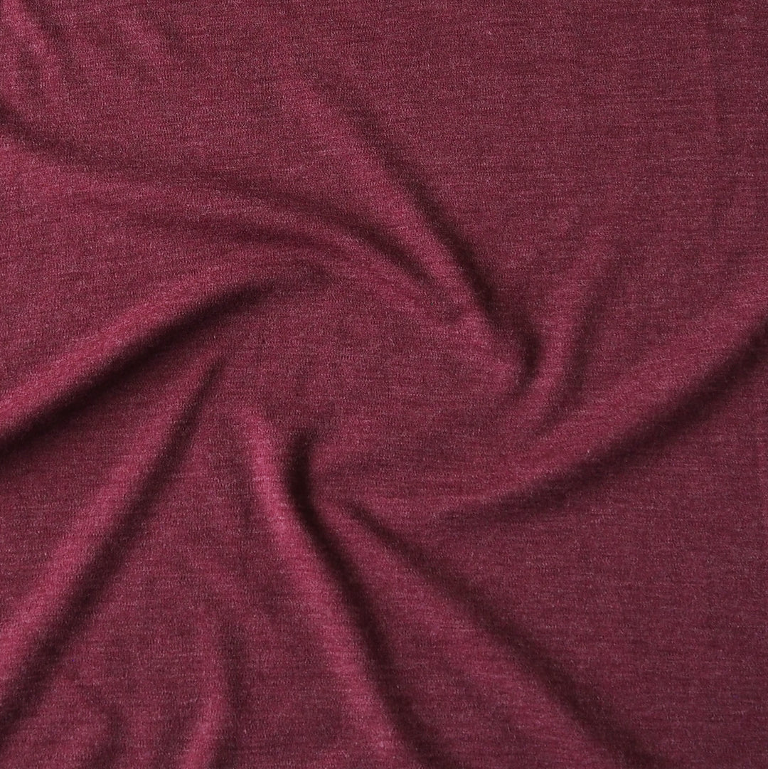 A close-up of draped heathered burgundy fabric with soft folds and a subtle textured weave.