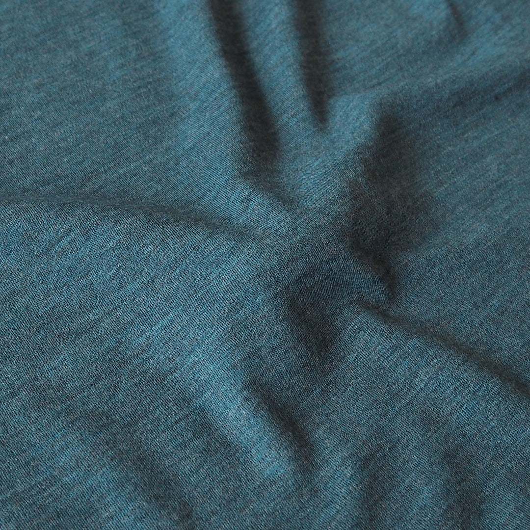 A close-up of a heathered teal blue fabric with soft folds and a fine knit texture.