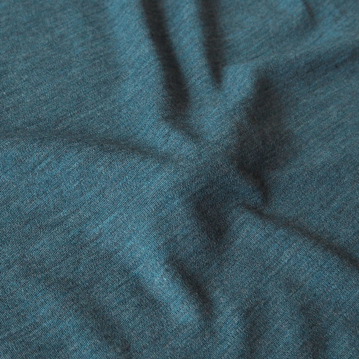 A close-up of a heathered teal blue fabric with soft folds and a fine knit texture.