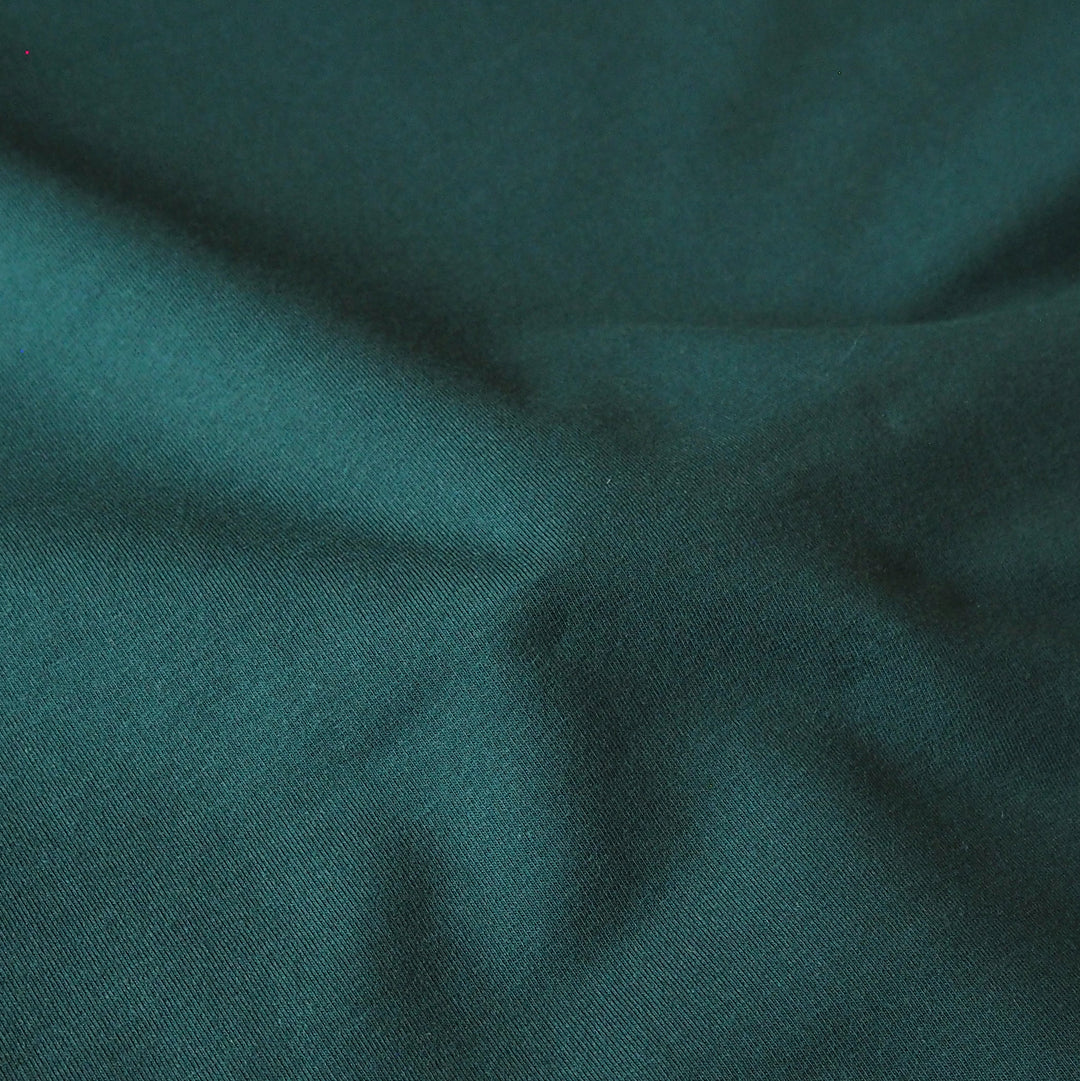 A close-up of dark teal green fabric with soft folds and a fine woven texture.