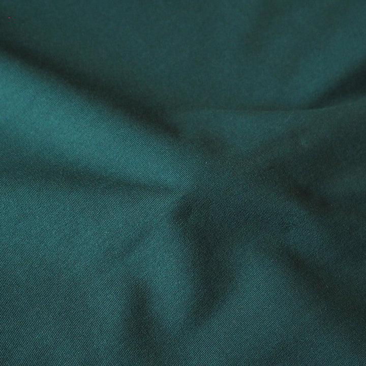 A close-up of dark teal green fabric with soft folds and a fine woven texture.